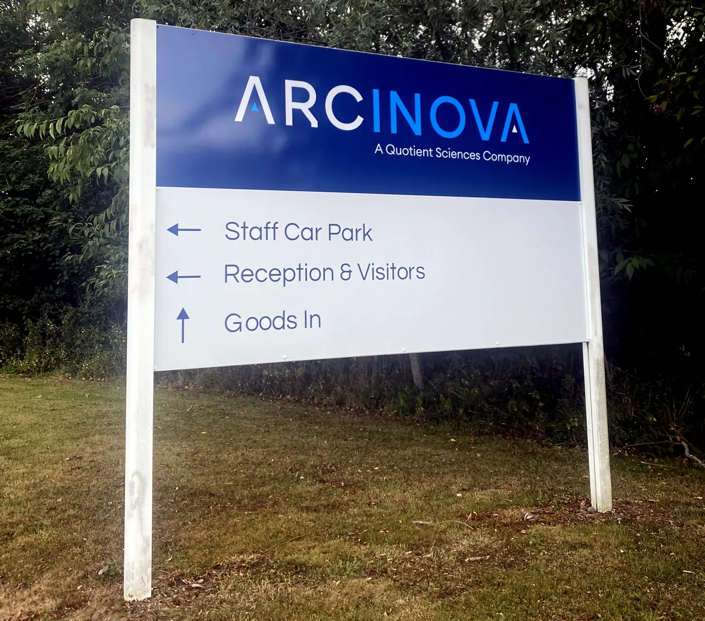 Post-mounted wayfinding sign for Arcinova showing staff car park, reception and goods in