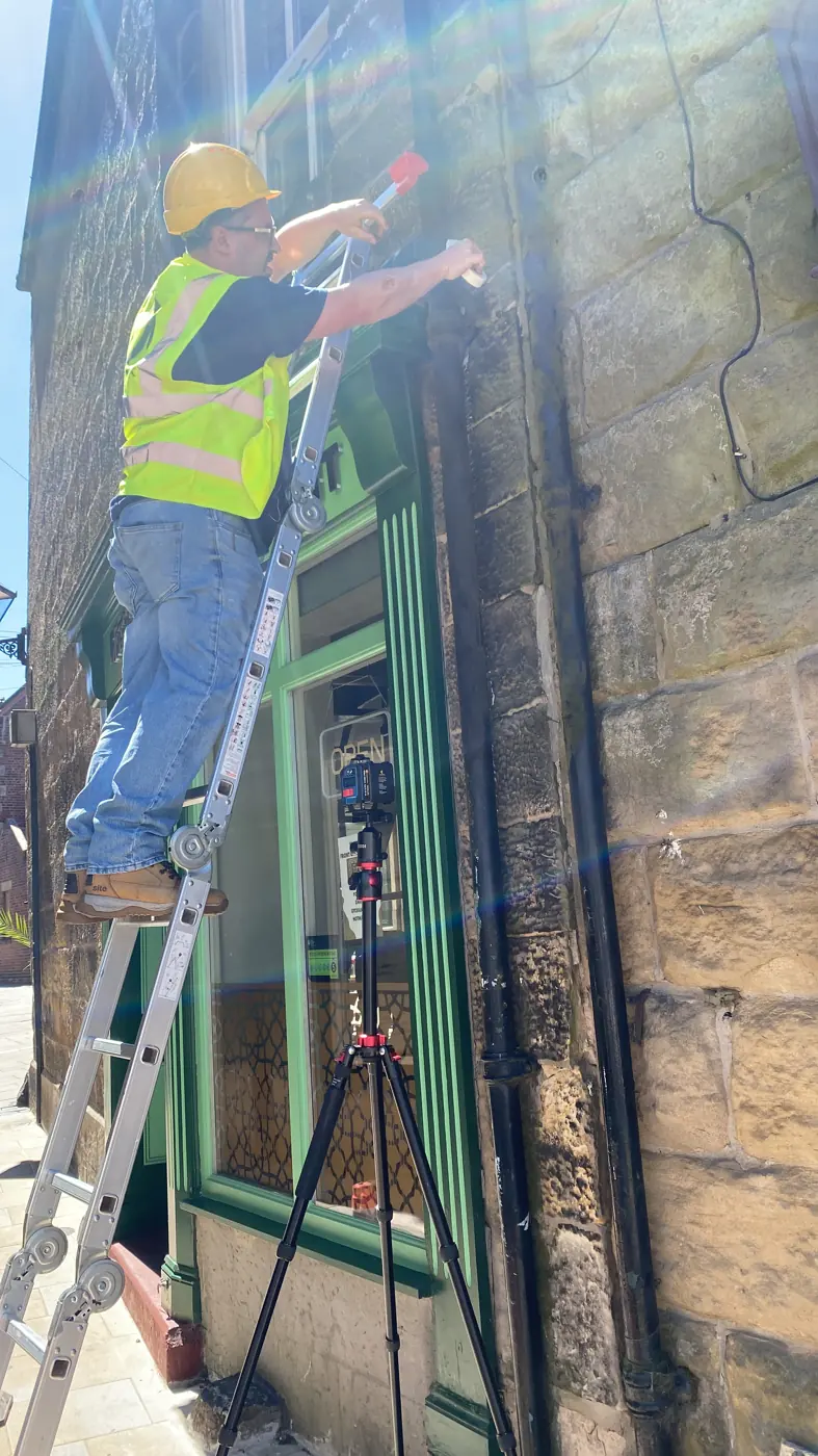 Fitter on a ladder fixing a sign to a stone shop front