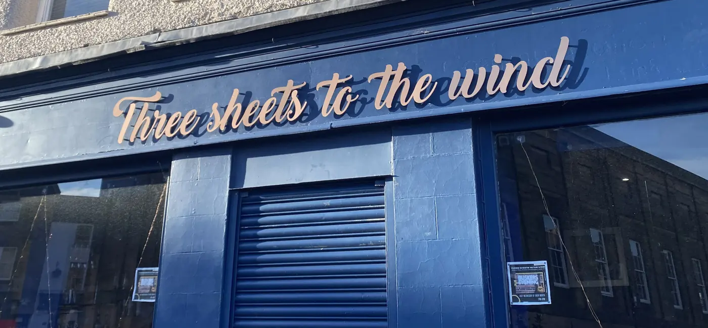 Gold built-up script letters on a navy fascia reading Three sheets to the wind